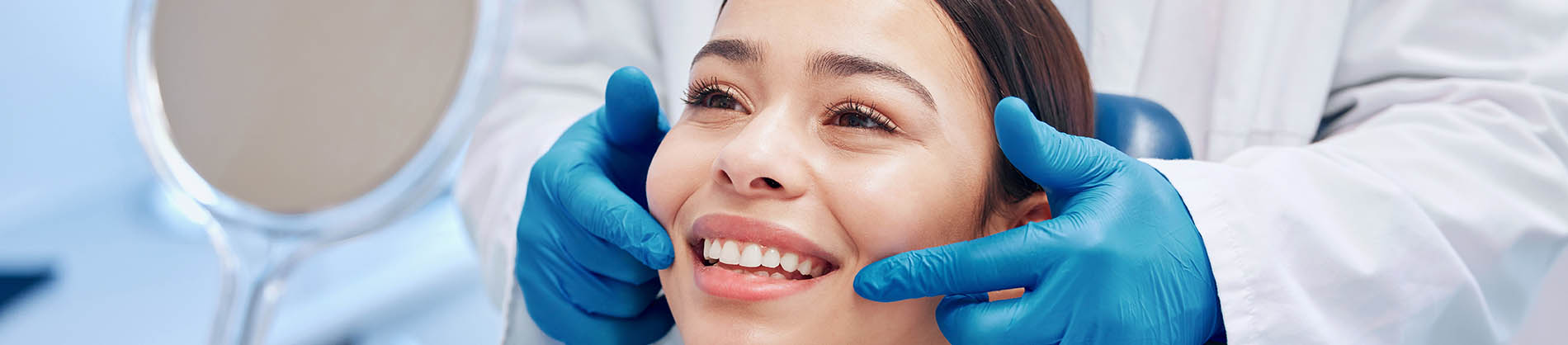 A person is seated in a dental chair, receiving care from a dental professional who stands behind them.